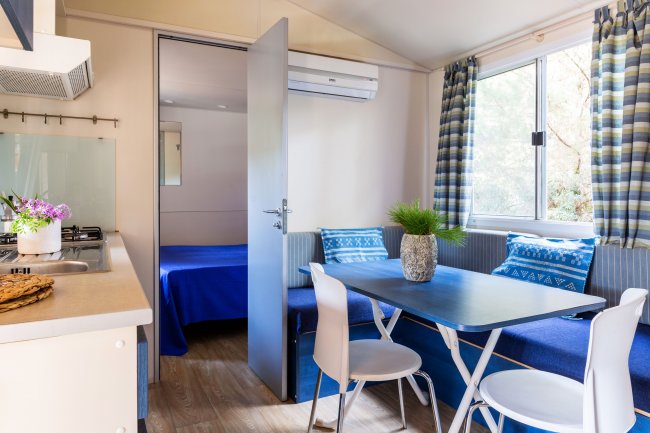 Interno di una casa mobile con zona pranzo, cucina e camera da letto, decorato con tocchi di blu.