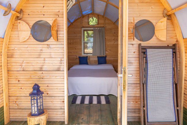 Interno di cabina di legno con letto, lampada blu e sedia pieghevole.