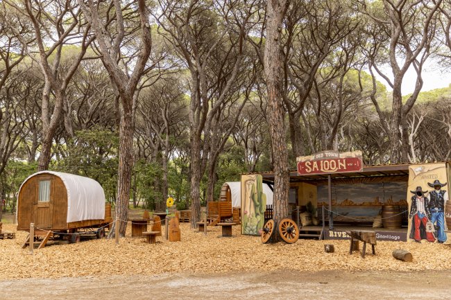 Strutture in stile western con carri coperti e un saloon tra alti alberi.