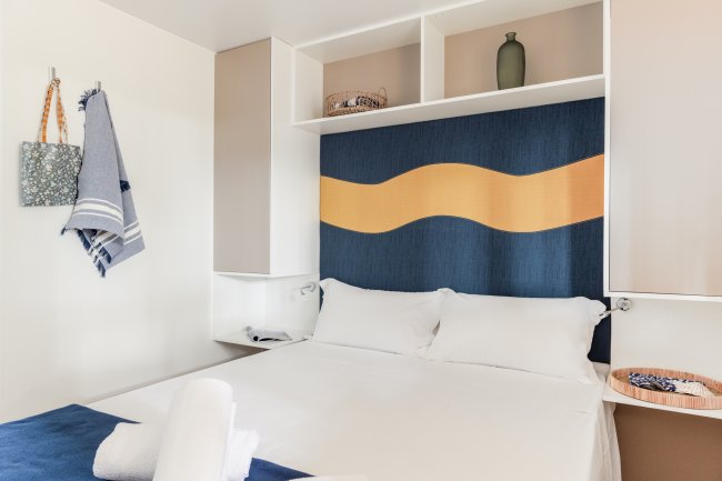 Una camera da letto con letto matrimoniale, cuscini bianchi e decorazione murale blu e arancione.