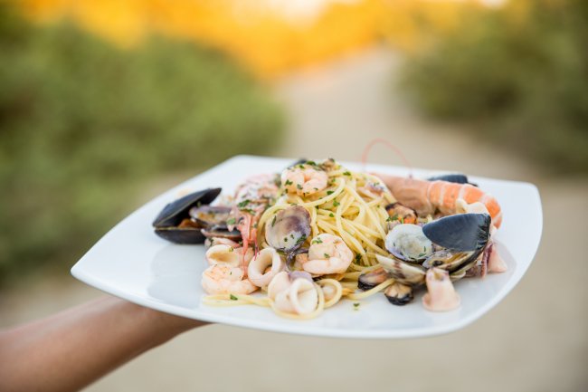 Un piatto di spaghetti ai frutti di mare con gamberi, cozze e calamari su un piatto quadrato.