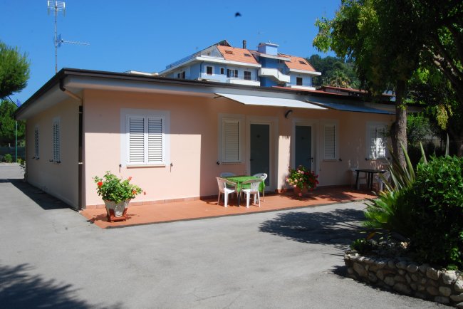 Esterno di una casa rosa con veranda e giardino.