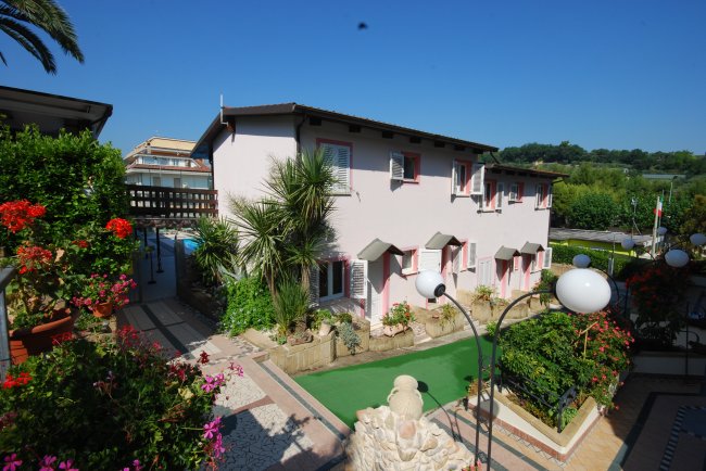 Edificio rosa con giardino fiorito e vialetto.