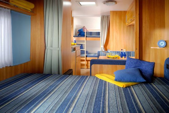 Interno di una casa mobile con letto matrimoniale, dinette e letti a castello.