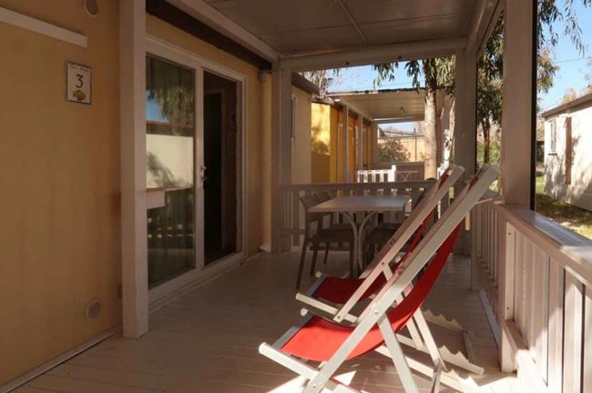 Veranda con sedie a sdraio rosse e tavolo bianco.