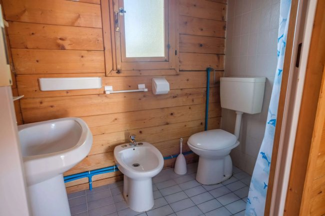 Bagno con pareti in legno, sanitari bianchi e doccia nascosta. Finestra con vetro opaco.