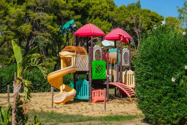 Parco giochi colorato con scivoli e tetti rossi immerso nella natura verde.