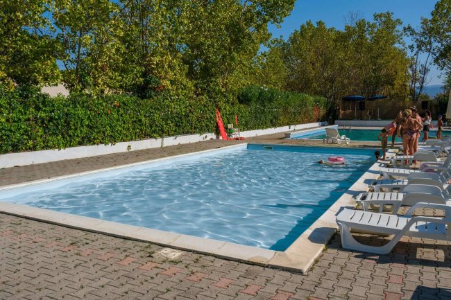 Piscine all'aperto con lettini bianchi e persone che si divertono sotto il sole.