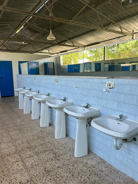 Diversi lavandini bianchi allineati in un bagno pubblico luminoso.