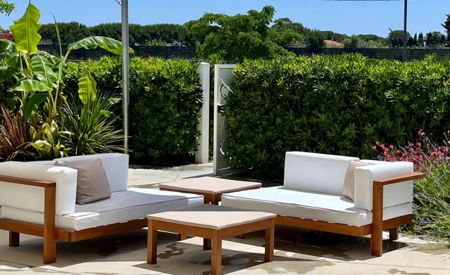 Area lounge esterna con divani bianchi e verde intorno.