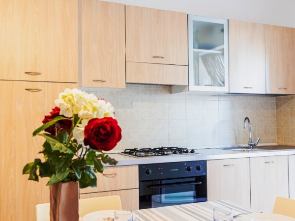 Cucina luminosa con fiori colorati in primo piano, mobili in legno e lavello.