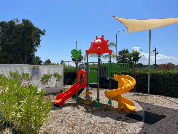 Parco giochi con scivoli colorati e una copertura in tela nel cielo azzurro.