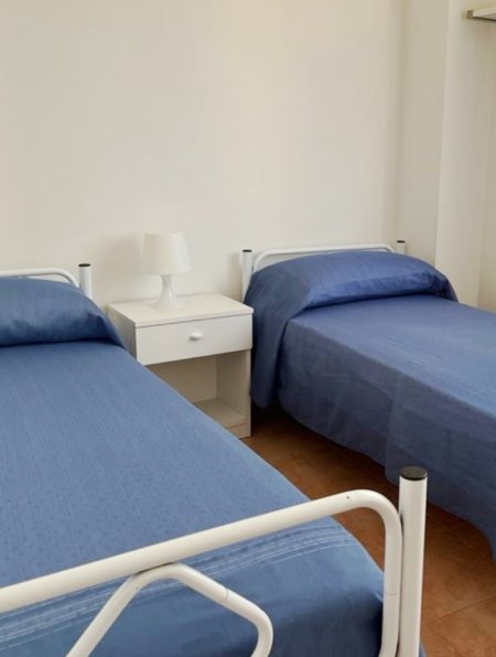 Camera con due letti singoli blu, comodino bianco e lampada.