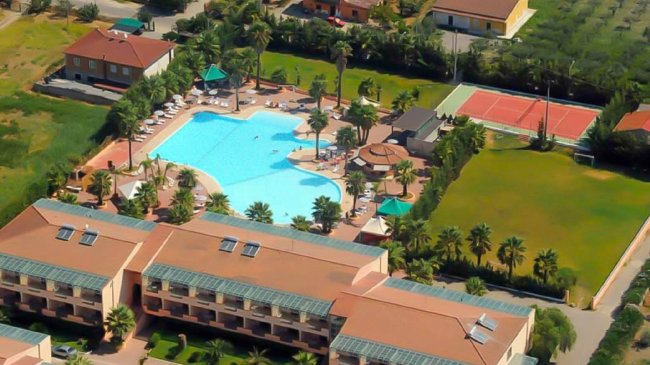 Vista aerea di una piscina con ombrelloni, campi sportivi e edifici attorno.