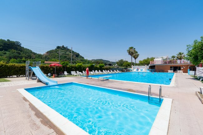 Piscine all'aperto con uno scivolo e sedie a sdraio, cielo sereno.