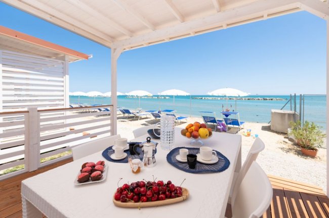 Tavolo apparecchiato sotto una veranda, vista sulla spiaggia e sul mare.