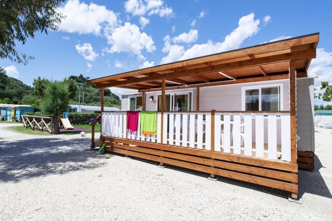 Casa mobile esterna con terrazza in legno e sedie bianche.