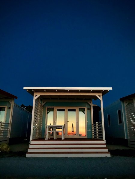 Una casetta in legno al tramonto, con tavolo e sedie in veranda, illuminata da un cielo notturno.