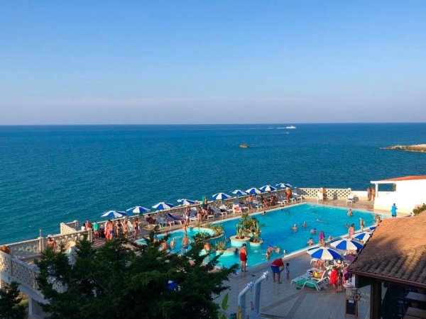 Piscina vista mare con ombrelloni blu e bianchi.