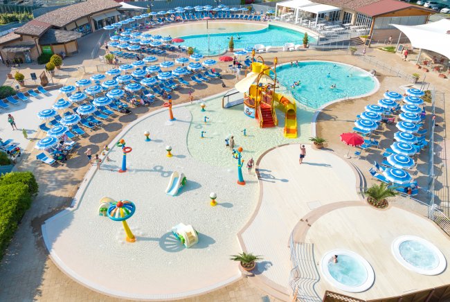 Parco acquatico con piscine, scivoli e ombrelloni blu.