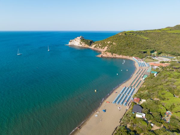 Spiaggia con file di ombrelloni azzurri, mare calmo e colline verdi.