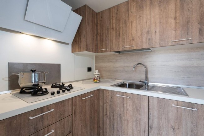Cucina moderna con mobili in legno, piano cottura a gas, cappa bianca e lavello in acciaio inox.