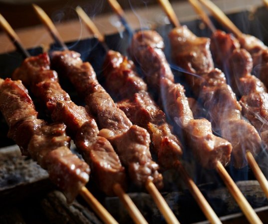 Spiedini di carne cotti alla griglia con fumo visibile.