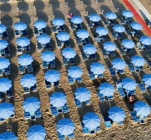 Vista dall'alto di una spiaggia con ombrelloni blu e sedie a sdraio.