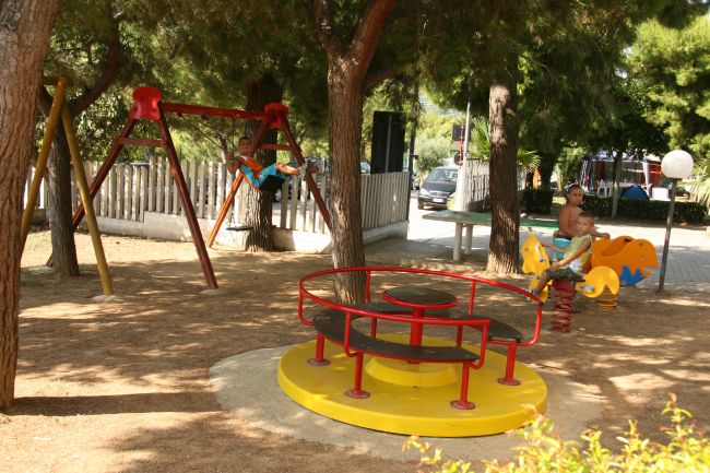 Un parco giochi con altalene, una giostra gialla e bambini che giocano tra gli alberi.