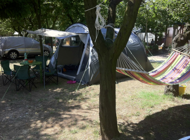 Campeggio con tenda, sedie, tavolo e amaca colorata tra gli alberi.