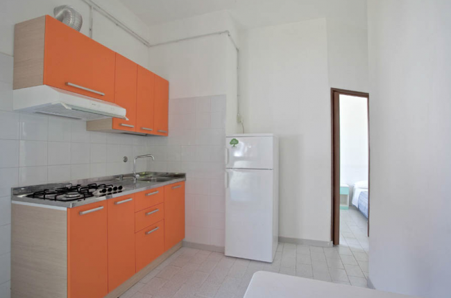 Cucina con mobili arancioni, fornelli a gas e frigorifero bianco.