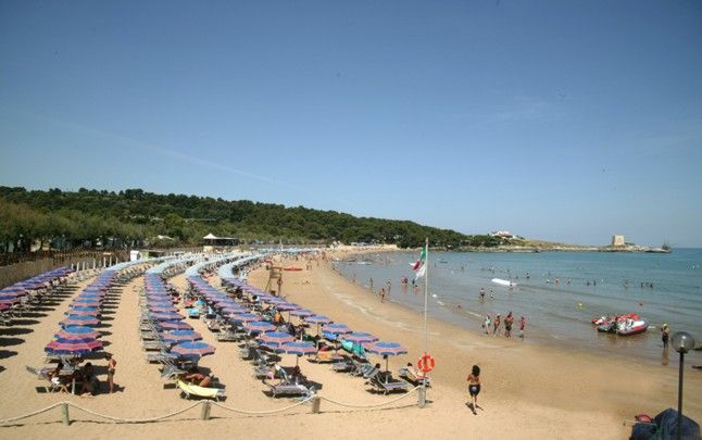 Spiaggia affollata con lettini e ombrelloni colorati, bagnanti in acqua.