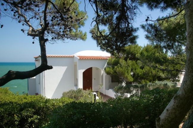 Casa bianca con tetto in tegole rosse, circondata da alberi, vista sulla costa.