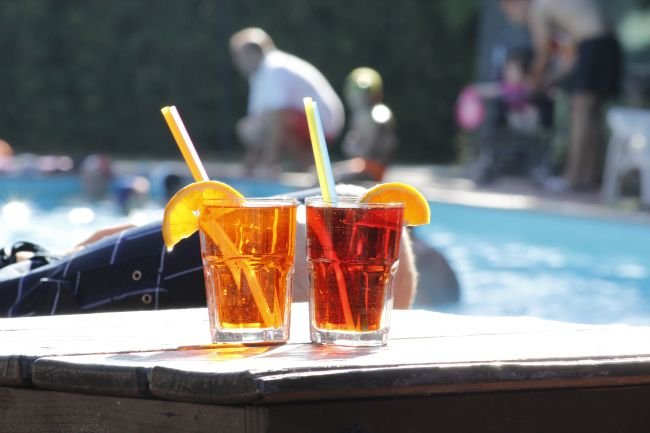 Due bevande rosse con fette d'arancia e cannucce, a bordo piscina.