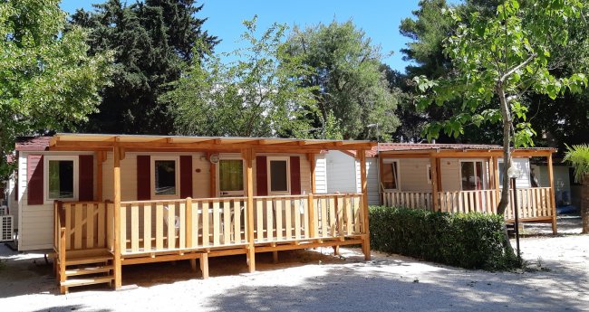 Bungalow in legno tra gli alberi, con veranda e porte-finestre.