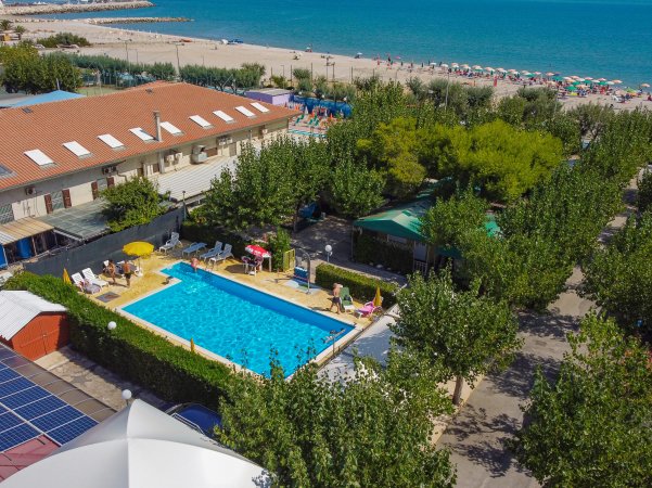 Vista aerea di una piscina vicino alla spiaggia, circondata da alberi e ombrelloni.