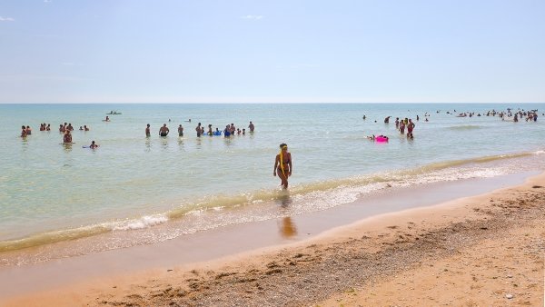 Spiaggia soleggiata con persone che nuotano e camminano vicino alla riva.
