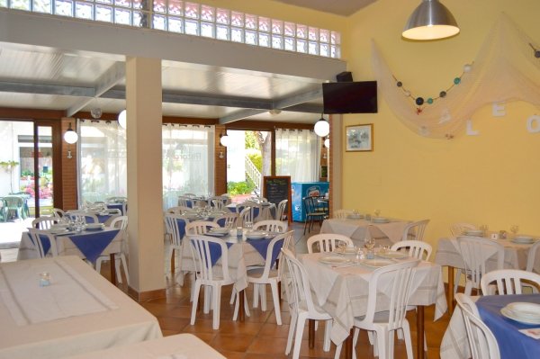 Ristorante con tavoli apparecchiati, sedie bianche, tovaglie bianche e blu.