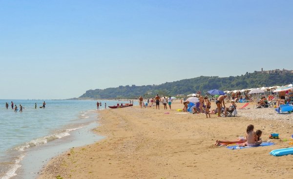 Spiaggia affollata con bagnanti e ombrelloni, colline verdi sullo sfondo.