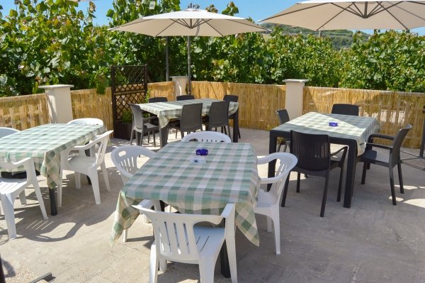 Terrazza all'aperto con tavoli apparecchiati, sedie bianche e nere, ombrelloni.