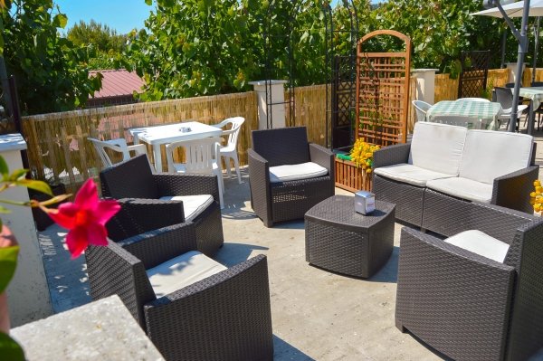 Area salotto su terrazza con poltrone nere, tavoli piccoli e piante decorative.
