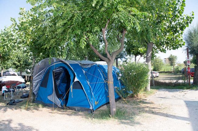 Una tenda blu piantata sotto alberi verdi in un campeggio, accanto a sedie da campeggio.