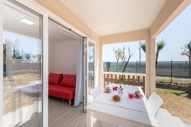 Terrazza con tavolo apparecchiato e soggiorno interno con divano rosso.