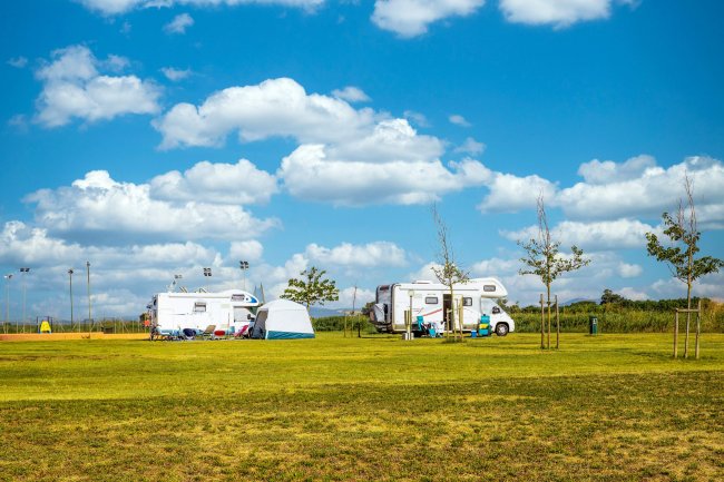 Due camper parcheggiati su un prato con una piccola tenda blu, sotto un cielo soleggiato con nuvole.