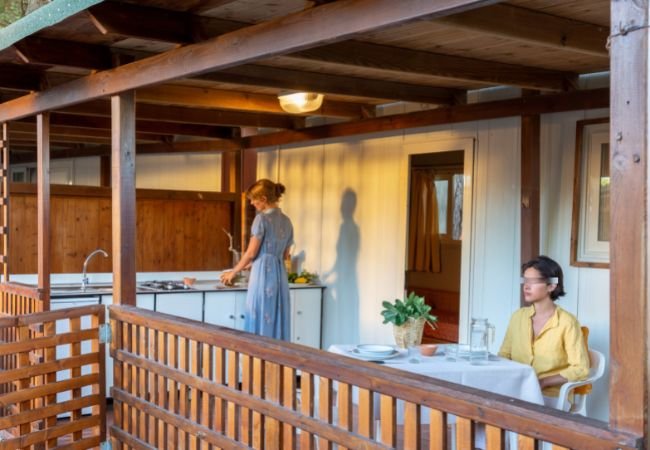 Due persone su una veranda, una cucina e l'altra sieda a tavola.
