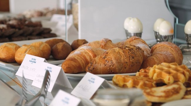 Tavolo della colazione con croissant, panini e waffle.