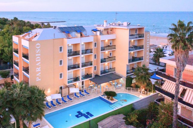 Hotel vista mare con piscina e palme verdi.