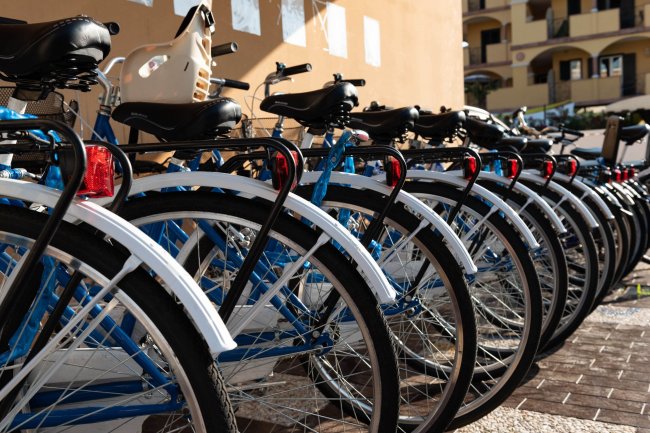 Biciclette blu allineate con parafanghi bianchi, edificio giallo sullo sfondo.
