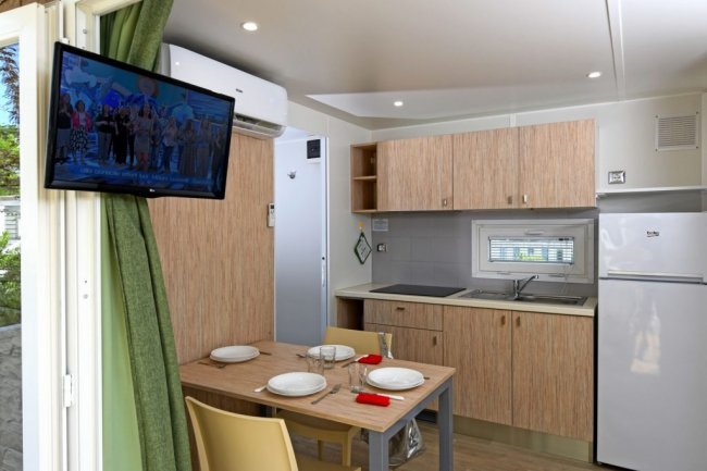 Cucina moderna con tavolo apparecchiato, TV a schermo piatto e frigorifero.