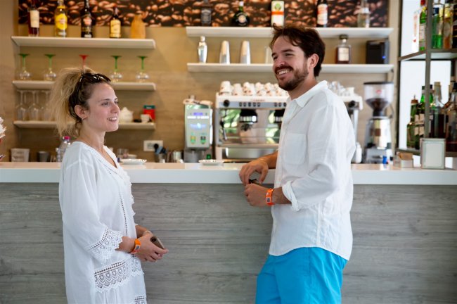 Due persone al bancone di un bar, sorridenti e vestite di bianco.